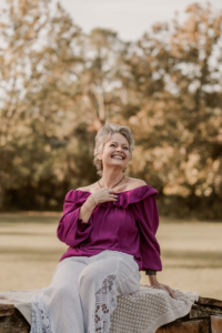Portrait of Tracy smiling in a park setting, seated outdoors and dressed professionally.