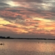 Sunset over a body of water with bright red, orange, and golden-yellow hues in the sky.