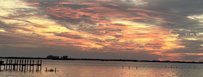 Sunset over a body of water with bright red, orange, and golden-yellow hues in the sky.